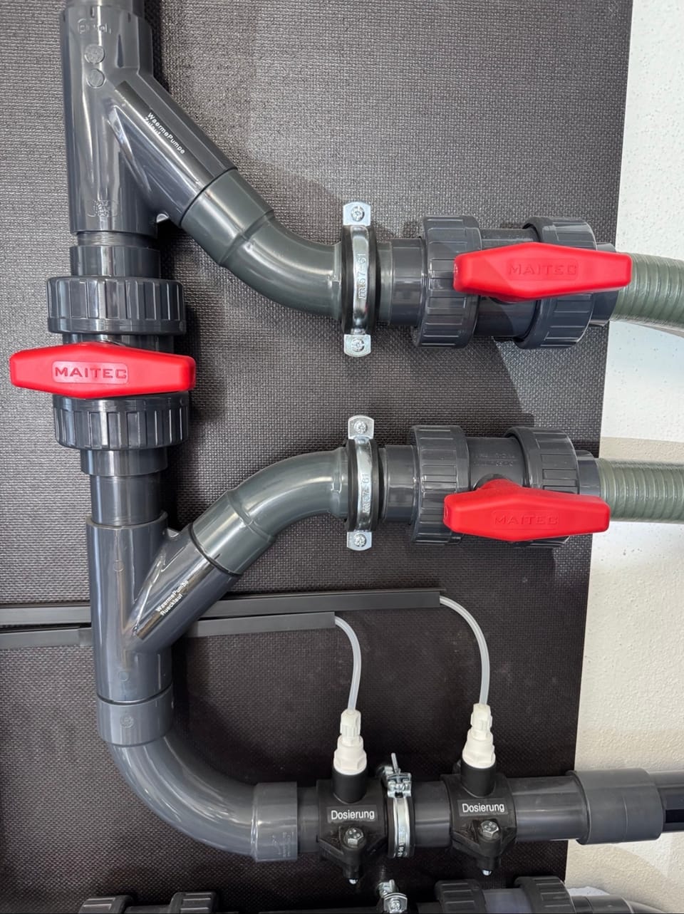 Detail eines Technikboards mit beschrifteten Anschlüssen für Wärmepumpe und Dosierung